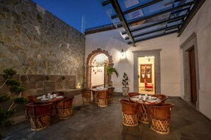 Un patio con muros de piedra, techo de vidrio y mobiliario exterior con mesas y sillas.