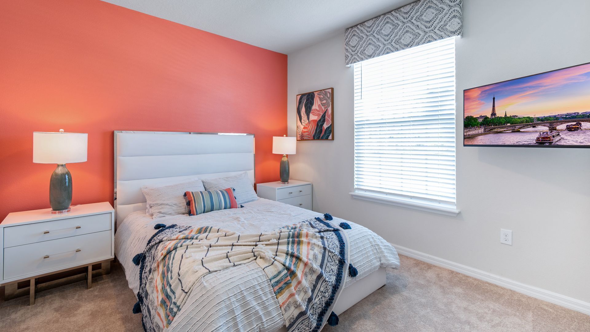 A bedroom with a bed, two bedside tables, a window with blinds, and a painting on the wall.
