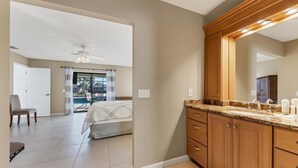 Une chambre dotée d’un grand lit, d’un ventilateur de plafond et offrant une vue sur une piscine grâce à une porte-fenêtre coulissante.