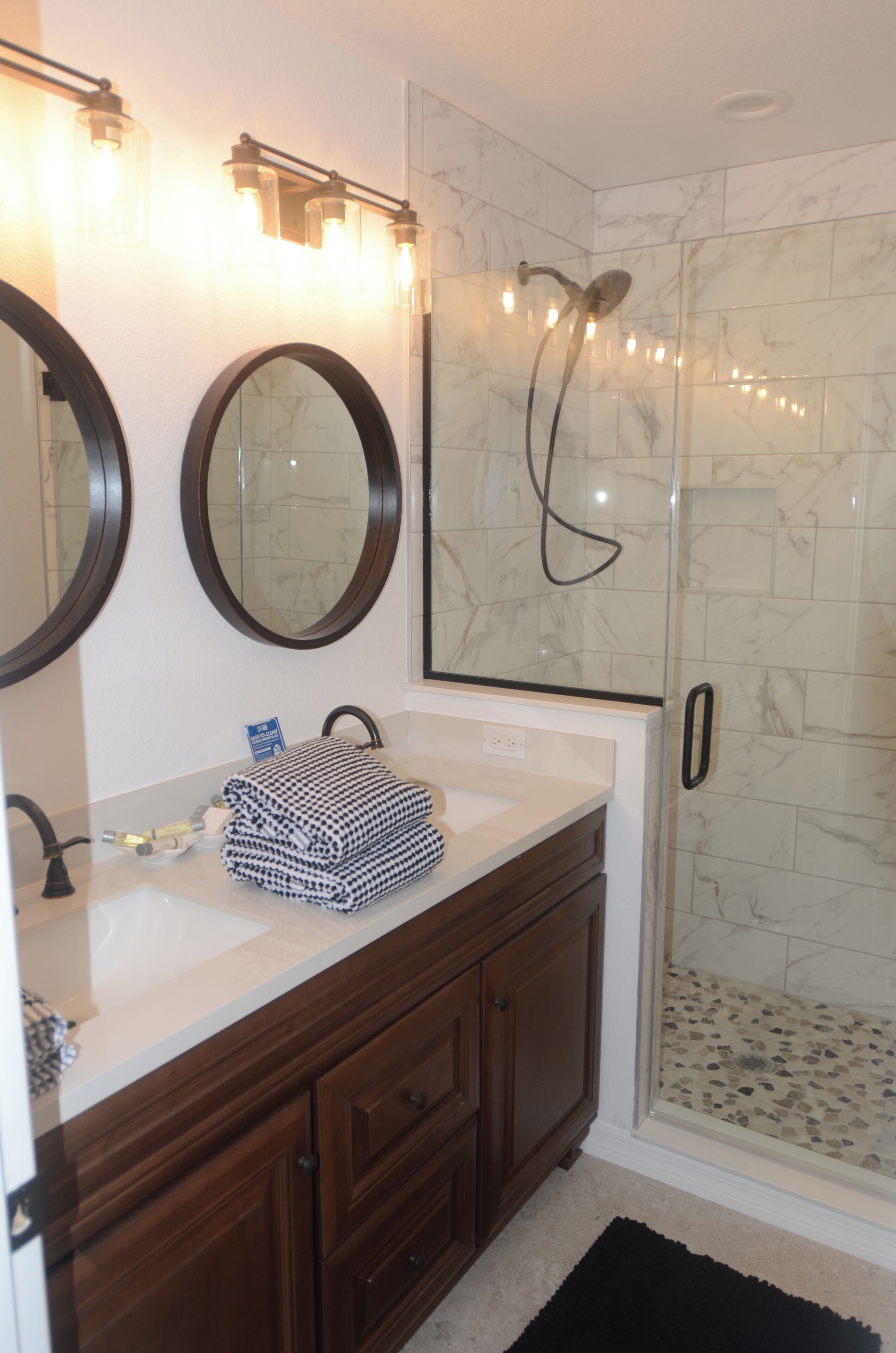 Een badkamer met een marmeren douche, een wastafel met een handdoek en twee spiegels.