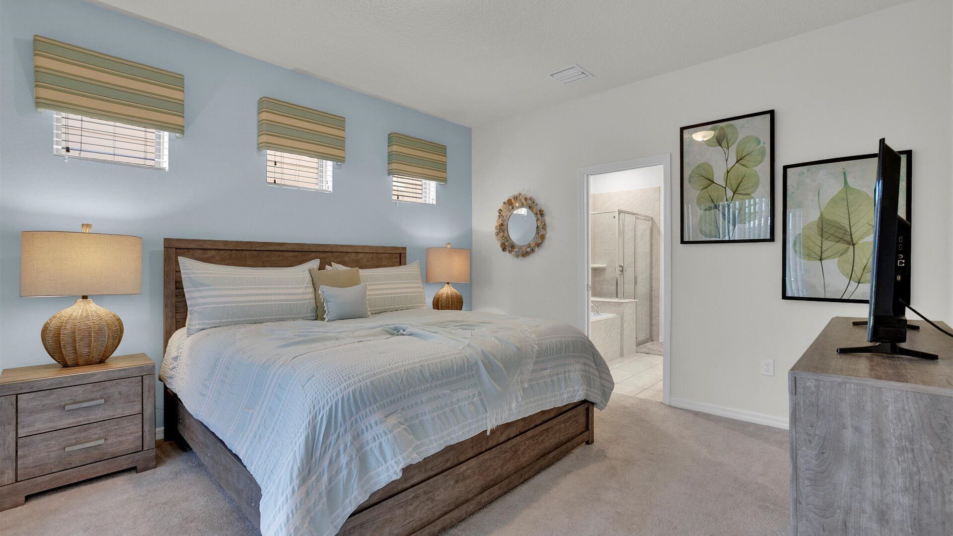 A bedroom with a bed, bedside lamps, a dresser, a television, and artwork on the walls.