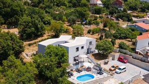 A modern house with a swimming pool, surrounded by trees and other houses.