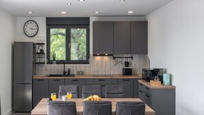 A modern kitchen with dark cabinetry, a wooden island, and a dining area with grey upholstered chairs.