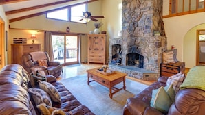 Una sala de estar acogedora con chimenea de piedra, sofás de cuero, una mesa de centro de madera y un ventilador de techo.