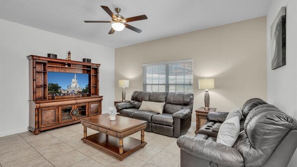 A living room with a wooden entertainment center, a ceiling fan, a large window with blinds, and two sofas. - New Listing! Paradise Palms Resort, 6mi to Disney & 14mi to Universal - GRH509175 (Kissimmee)