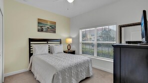 A bedroom with a bed, a nightstand, a lamp, a dresser, a mirror, and a window with blinds. - New Listing! Paradise Palms Resort, 6mi to Disney & 14mi to Universal - GRH509175 (Kissimmee)