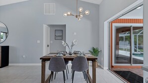 A dining area with a table set for two, a modern chandelier, and a view of a pool through glass doors. - New Listing! Charlotte Harbor Area Resort, 120mi to Disney & 134mi to Universal - GRH518223 (Englewood)