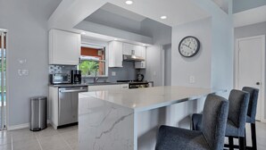 A modern kitchen with white cabinets, a marble island, and a clock on the wall. - New Listing! Charlotte Harbor Area Resort, 120mi to Disney & 134mi to Universal - GRH518223 (Englewood)