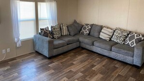 Un salón con un sofá modular gris, almohadones estampados, suelo de madera con diseño de espiga y una lámpara en el techo.