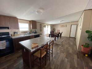 A kitchen with wooden cabinets, a granite countertop, a built-in stove, and a dining area with a table and chairs. - 3/4 Acre DoubleWide Mobile Home 7 minutes To Circus of America (Del Valle)