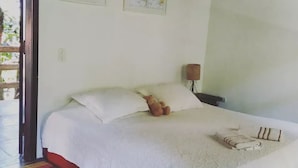 Un dormitori amb un llit, almoines, una làmpada i una manta amb ratlles de colors.