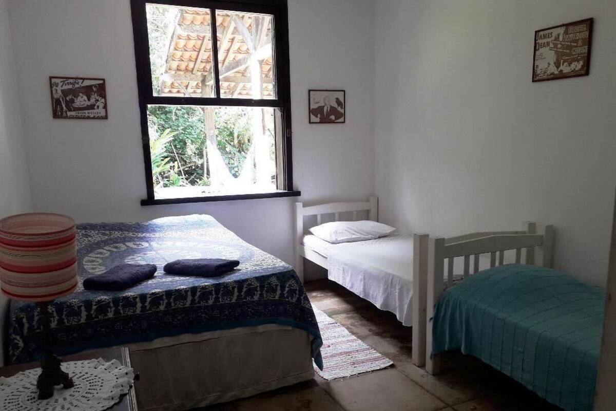 A bedroom with two beds, a window with a view of greenery, and a small table with a decorative item.