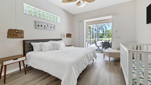 Une chambre moderne avec un grand lit, une table de chevet en bois, une lampe en osier et une vue sur un balcon aménagé avec du mobilier d’extérieur.