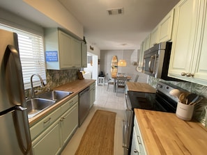 A modern kitchen with light green cabinets, stainless steel appliances, a wooden countertop, and a dining area with a table and chairs. - Ocean Beach Cottage (Palm Coast)