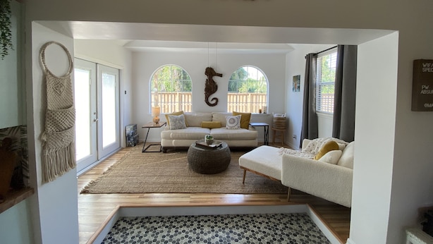 A spacious living room with a large window, a sofa, a coffee table, and a macrame wall hanging. - Ocean Beach Cottage (Palm Coast)