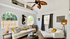 A spacious living room with a high ceiling, a large window, and a ceiling fan. - Ocean Beach Cottage (Palm Coast)