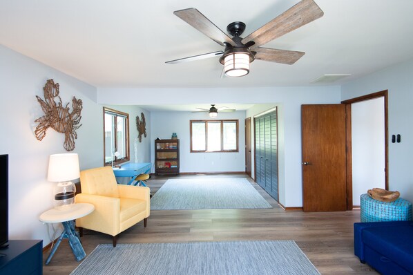 A spacious living room with a ceiling fan, a sofa, a coffee table, and a television. - Stylish Home on the Choptank River (with Tidal Beach) (Preston)