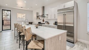 Una cucina moderna con una grande isola, elettrodomestici in acciaio inossidabile e un'area pranzo con sgabelli da bar.