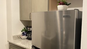 A kitchen with a stainless steel refrigerator, granite countertop, and light-colored cabinets. - Modernized Studio Apartment in Gadsden, AL (Gadsden)