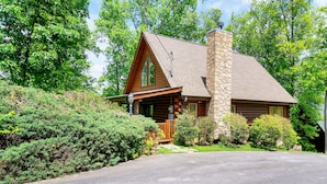 A log cabin with a stone chimney, wooden porch, and a stone wall. - Great Cabin sleeps 8, New Furnishings, Loft w/ Arcade Games, Hot Tub & Fireplace (Sevierville)