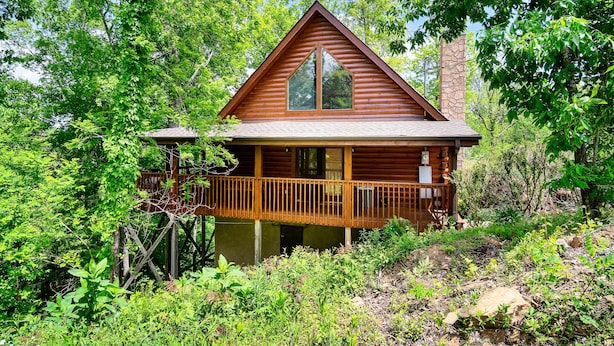 A cabin with a wooden exterior, a balcony, and a stone chimney. - Great Cabin sleeps 8, New Furnishings, Loft w/ Arcade Games, Hot Tub & Fireplace (Sevierville)