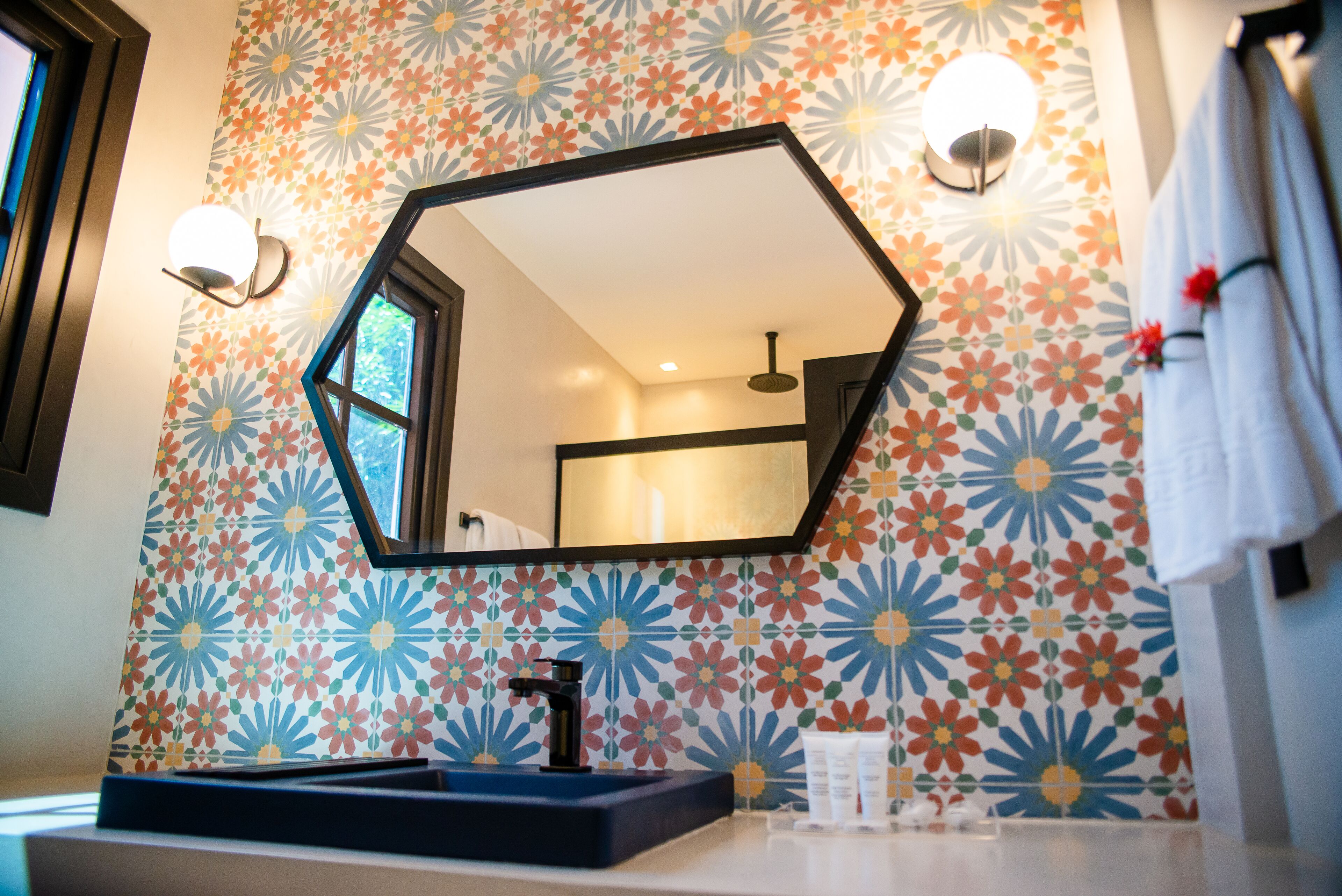 A bathroom with a hexagonal mirror, a sink, and a floral-patterned wall.