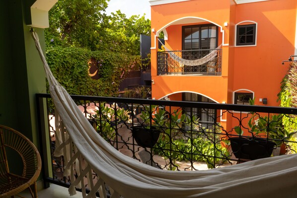 Una hamaca en un balcón con vistas a un edificio naranja y vegetación.