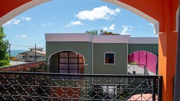 A view through a metal gate of a building with a green facade, a pink awning, and a small window.