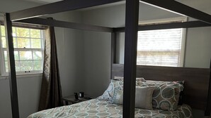 A four-poster canopy bed with a patterned bedspread, a bedside table, and a window with curtains. - Park-like and sports bar - close to MSU (Lansing)