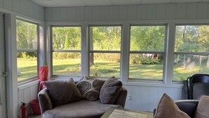 A cozy room with a cushioned seating area, large windows, and a view of a grassy yard. - Park-like and sports bar - close to MSU (Lansing)