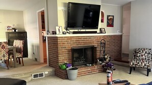 A living room with a fireplace, a television, a sofa, and a coffee table. - Park-like and sports bar - close to MSU (Lansing)