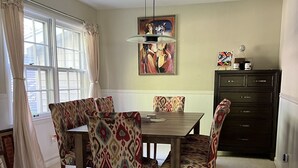A dining area with a table and chairs, a painting on the wall, and a cabinet. - Park-like and sports bar - close to MSU (Lansing)