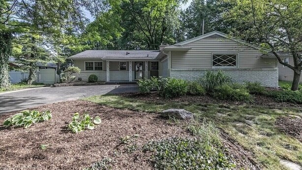A single-story house with a front porch, a garage, and a well-maintained lawn with mulch and small plants. - Park-like and sports bar - close to MSU (Lansing)