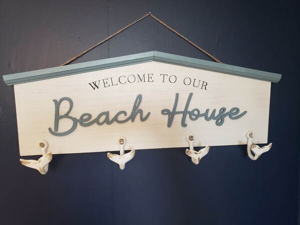 A wooden sign with the text 'WELCOME TO OUR Beach House' and four white bird-shaped hooks. - Sleeps 6, + 2 in Basement, Super Clean, Long Driveway, Fenced Yard w/Fire Pit (Port Clinton)