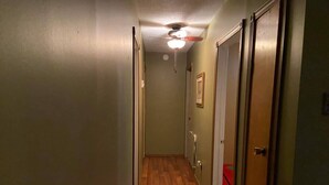 Um corredor estreito com piso de madeira, ventilador de teto e uma porta no final.