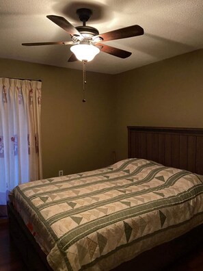 A bedroom with a bed, a ceiling fan, and a window with curtains.