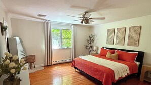 Um quarto com uma cama, um ventilador de teto, uma janela com cortinas e um espelho fixado na parede.