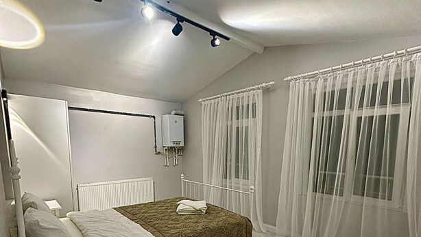 A bedroom with a bed, bedside table, radiator, and a window with sheer curtains. - Ortaköy Tiny One (Istanbul)