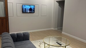 A modern living room with a sectional sofa, a glass coffee table, and a flat-screen TV mounted on the wall. - Ortaköy Tiny One (Istanbul)