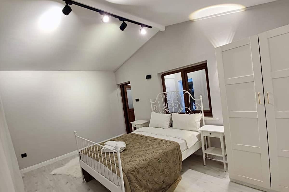 A bedroom with a bed, bedside table, wardrobe, and a sloped ceiling with track lighting.