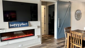 A modern living room with a fireplace, a flat-screen TV, and a dining area with wooden chairs and a table. - Possum Kingdom Lake Luxury, Upgraded Lakefront Condo w Breathtaking Water View (Graford)