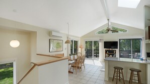 A spacious kitchen with a dining area, large windows, and a ceiling fan. - Chappy - Family Beach House (Edgartown)