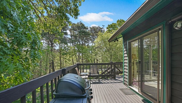 A wooden deck with a grill, a glass door leading to a covered area, and a view of trees and sky. - Chappy - Family Beach House (Edgartown)