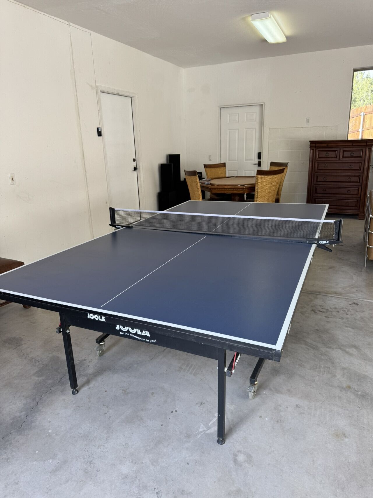 Ein Tischtennistisch in einem Raum mit Betonboden, weißen Wänden und einem Holzschrank.