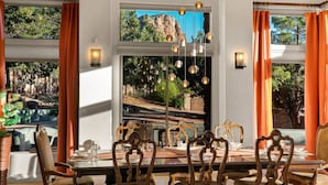 A dining area with a large window overlooking a scenic landscape, ornate wooden chairs, and a chandelier. - 206A&B Lake Dr Entire Home · Luxury Home; Spa, Fireplaces, Gourmet Kitchen (Sedona)