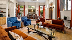 A spacious living room with a large sofa, armchairs, and a coffee table. There is a dining area with a chandelier and red curtains. - 206A&B Lake Dr Entire Home · Luxury Home; Spa, Fireplaces, Gourmet Kitchen (Sedona)
