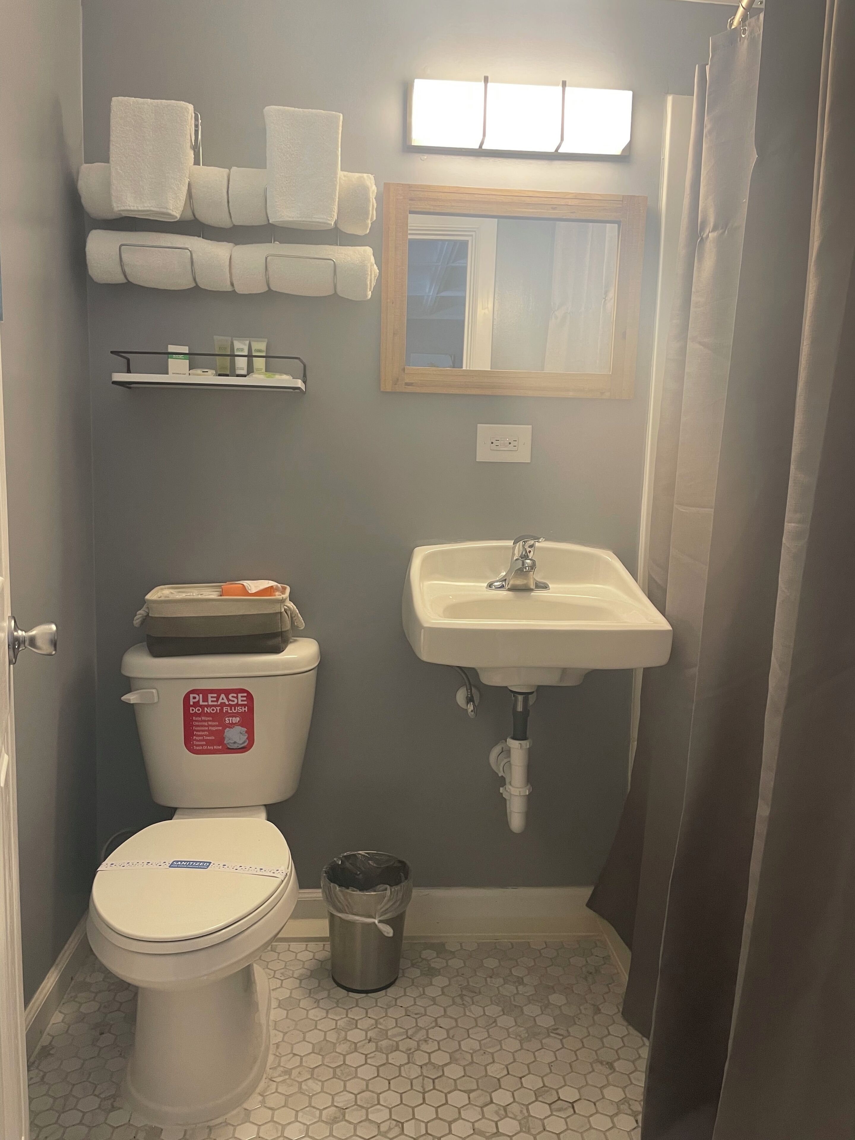 A bathroom with a toilet, sink, and a trash can. There are towels on a rack and a shower curtain.