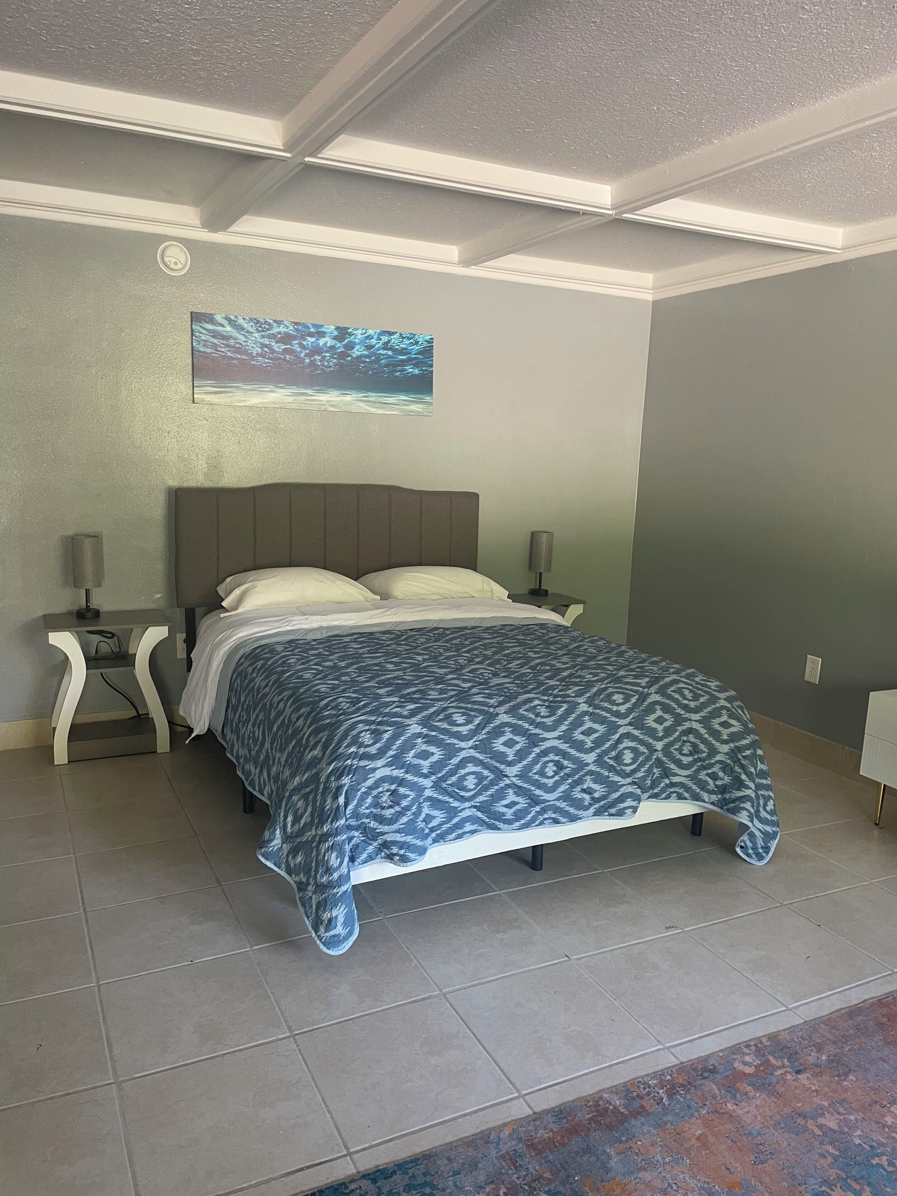 A bedroom with a bed, nightstands, a ceiling light, and a wall-mounted projector.