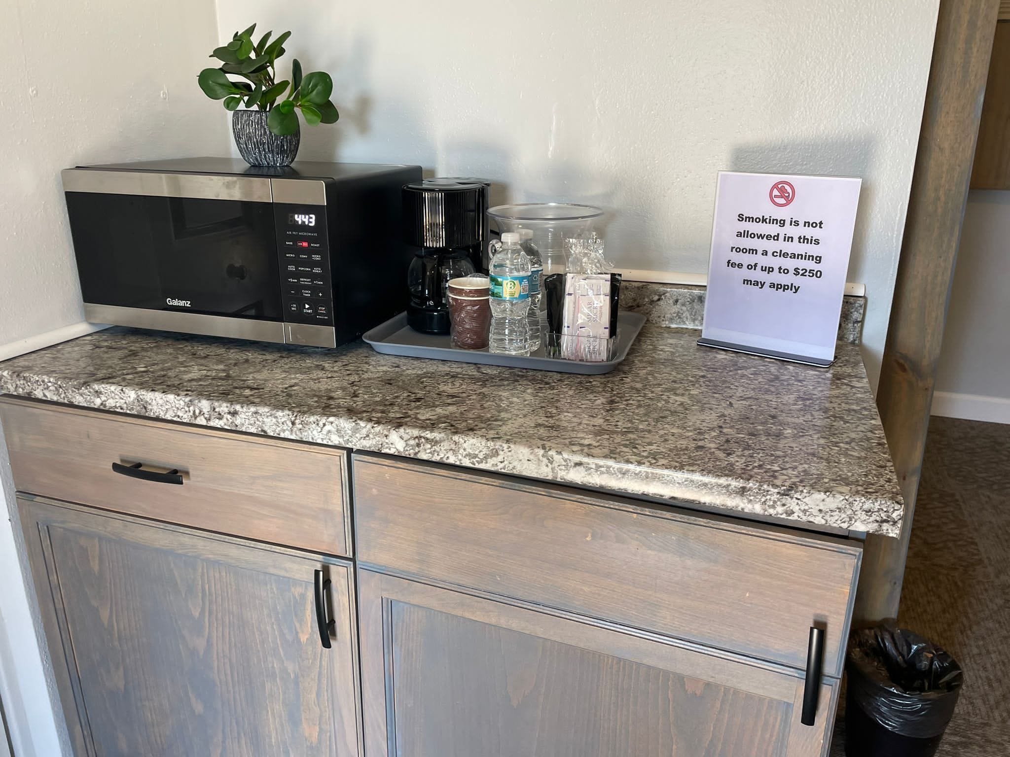 A kitchenette with a microwave, coffee maker, and a tray with water bottles and snacks. A sign indicates a smoking fee of up to $250.