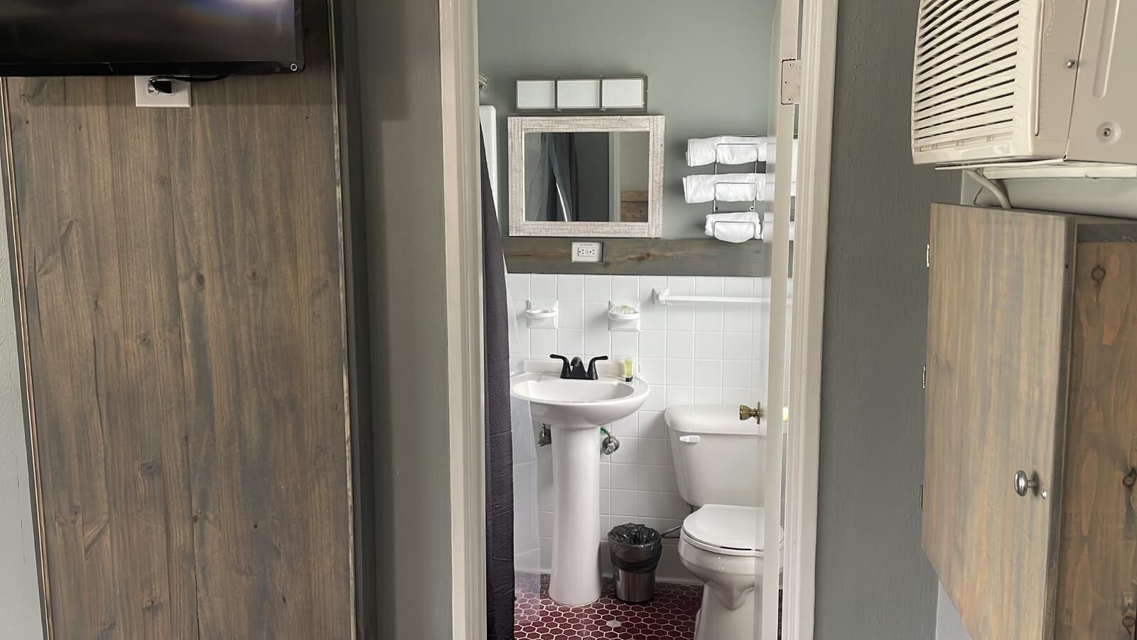 A bathroom with a wooden floor, a white sink, a toilet, and a mirror above the sink.